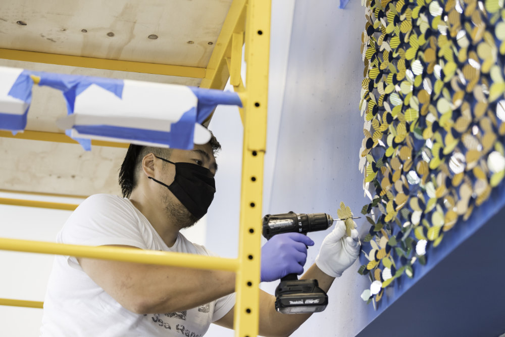Jay Yan wears a mask while on a scaffold drilling discs into the wall.