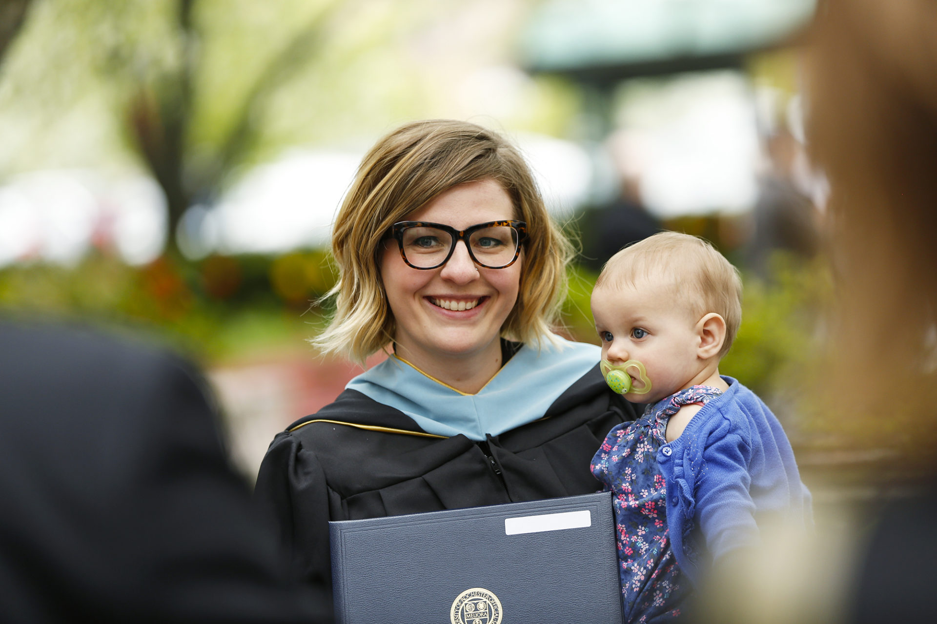 A Warner School of Education graduate poses for a photo holding her diploma and her child