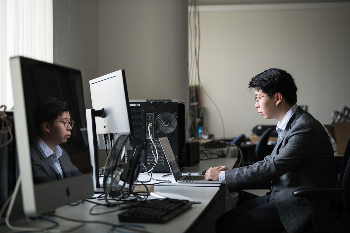 Man working on a laptop at a desk in an office filled with electronic devices and cables.