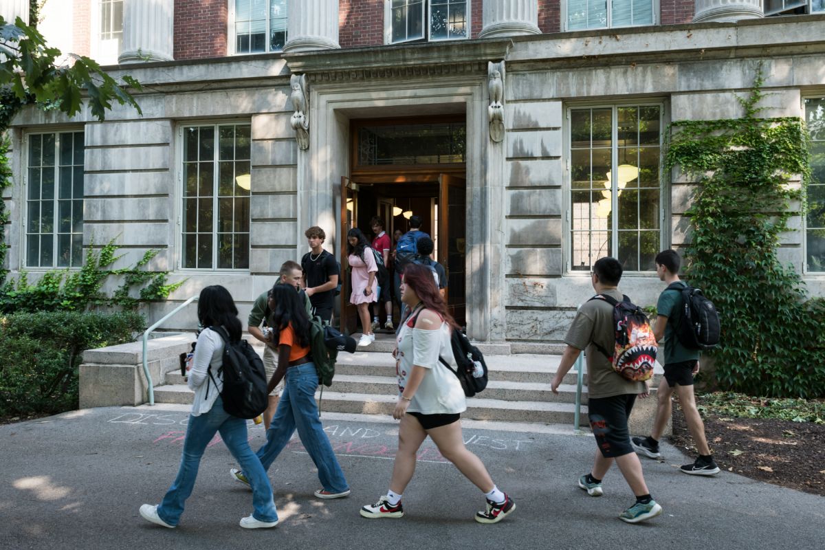 Students walk in and out of a classical academic building entrance with large windows and columns.