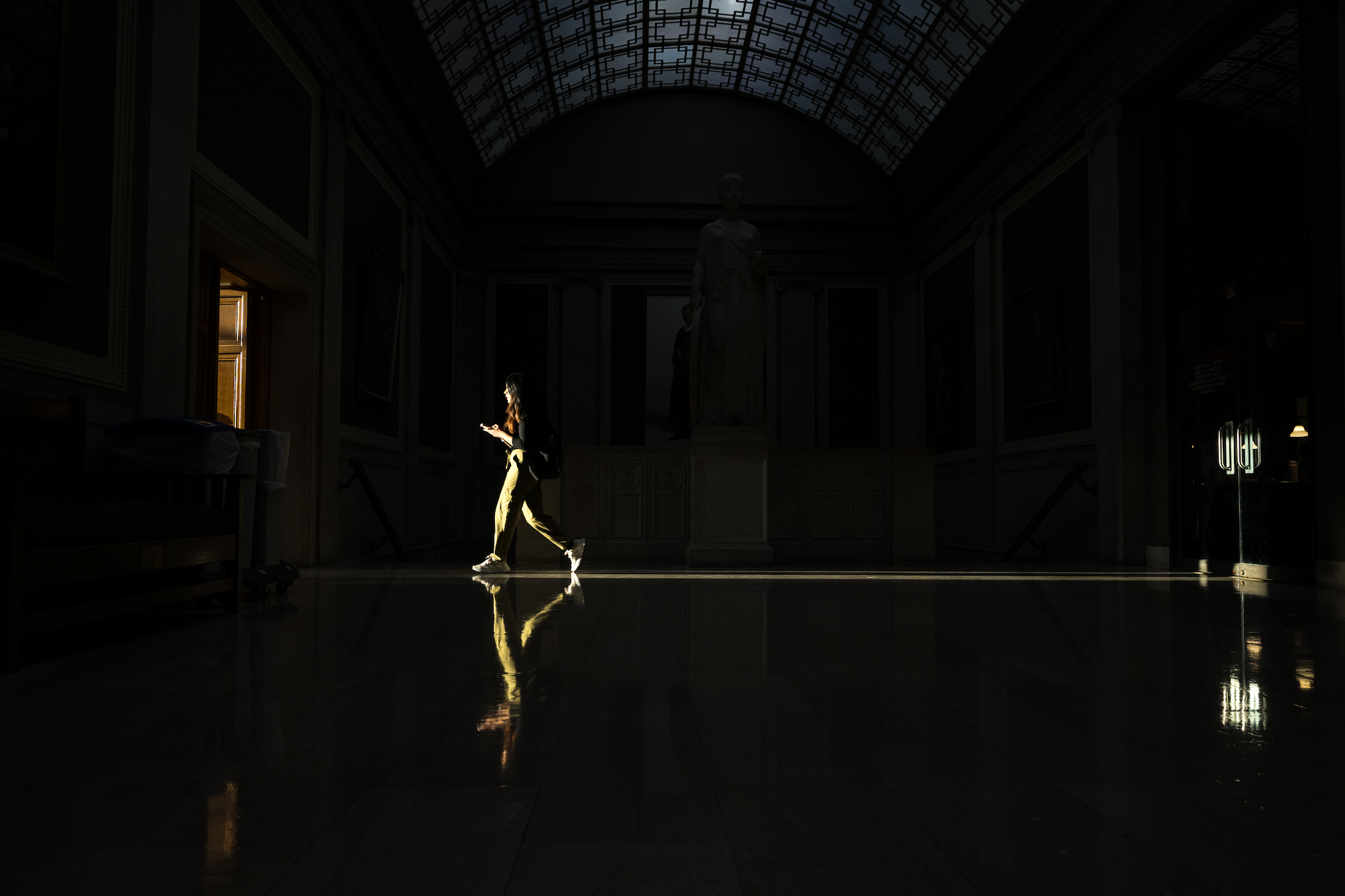 Evening sunlight shines through a doorway from Messinger Periodical Room into the Great Hall of Rush Rhees Library. Student is illuminated by the sunlight