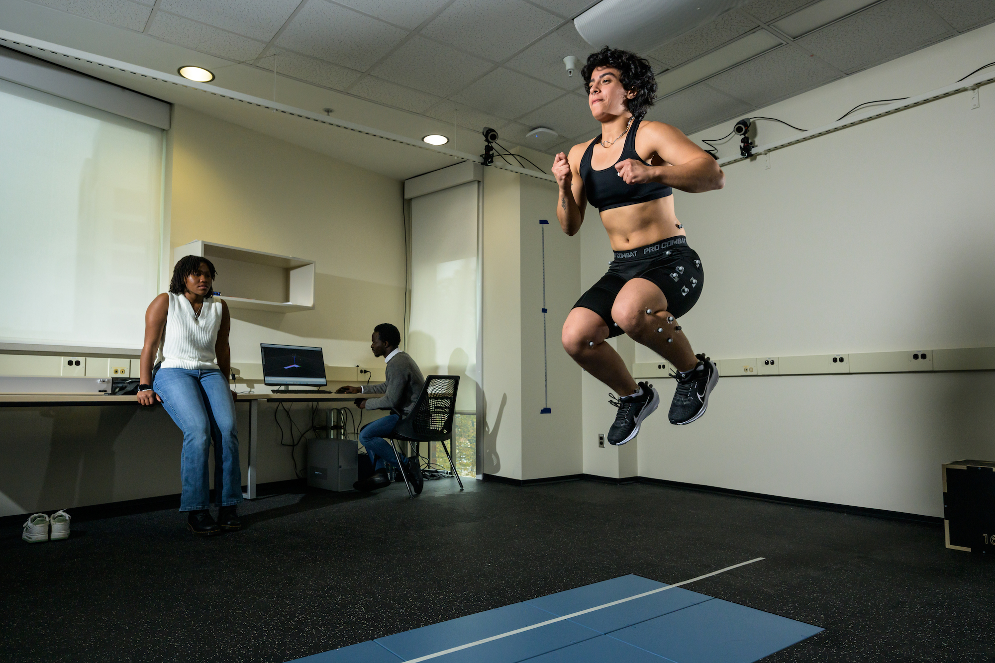 Student performs various movement and balance tasks on a force plate walkway while wearing shoes instrumented with pressure insoles and a suit outfitted with reflective markers