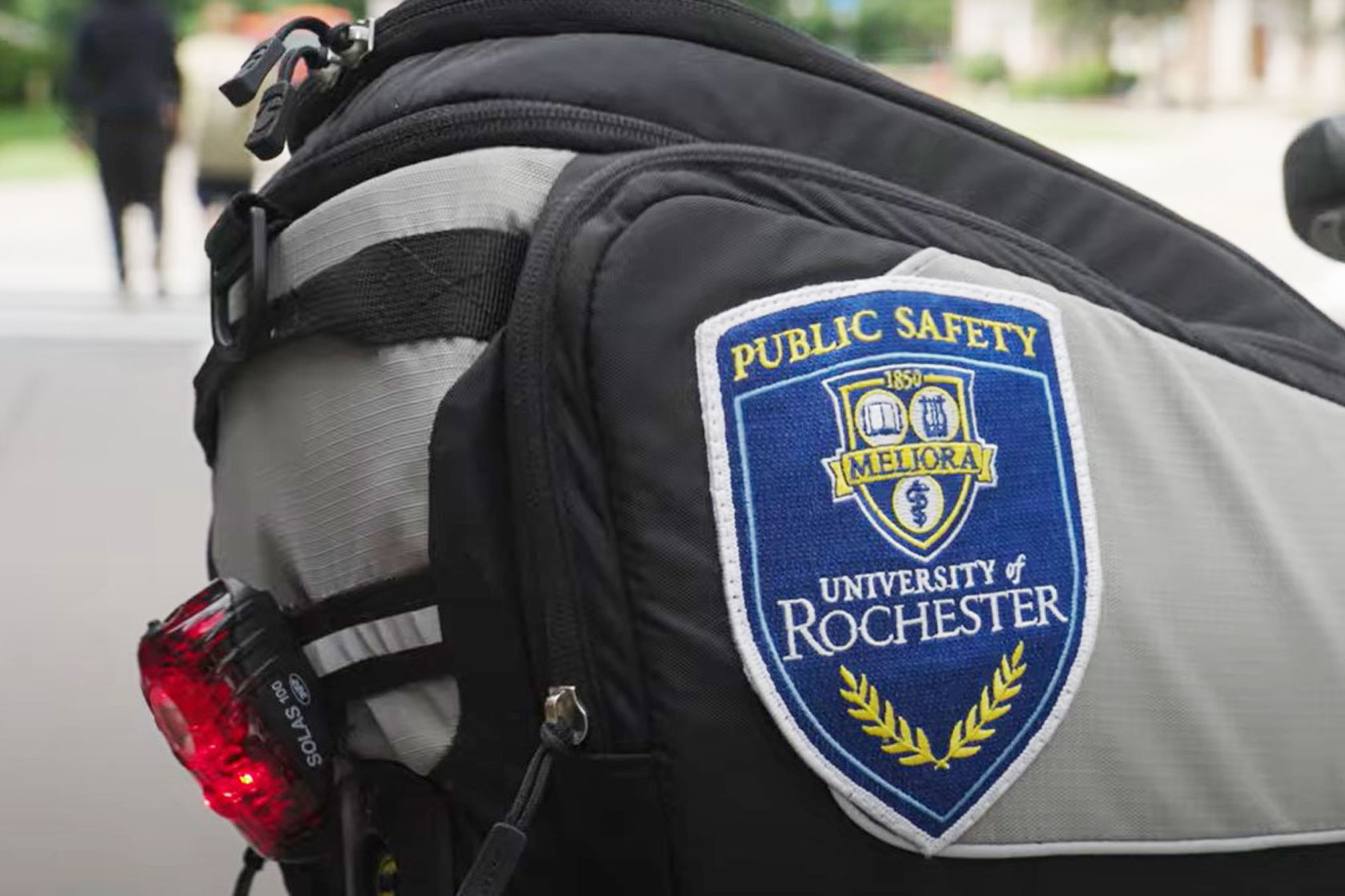 Close-up of a backpack with a "Public Safety, University of Rochester" patch and a red bike light.
