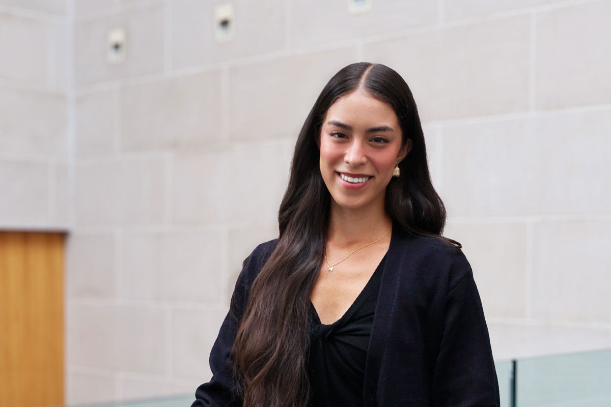 A woman with long hair in a black top smiles warmly, representing the vibrant community at the University of Rochester.